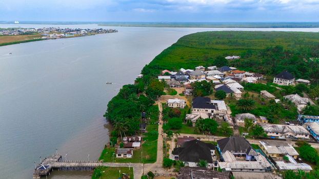 Aerial view of a coastal settlement featuring houses lush greenery a pier extending into the river and boats on the water in Minima Rivers Nigeria.