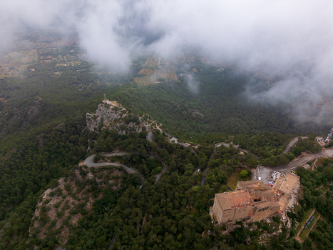 Aerial view of the Sanctuary of Sant Salvador on a mountain peak surrounded by winding roads and dense forest under low clouds in Felanitx Illes Balears Spain. Aerial view of the Sanctuary of Sant Salvador on a mountain peak surrounded by winding roads and dense forest under low clouds in Felanitx Illes Balears Spain.