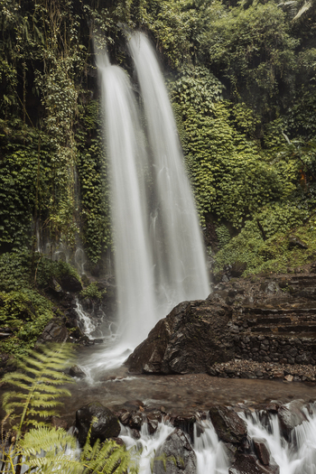 View of Grojogan Sewu Loket 2 waterfall with twin streams cascading down lush green cliffs into a rocky stream in Kecamatan Tawangmangu Jawa Tengah Indonesia.