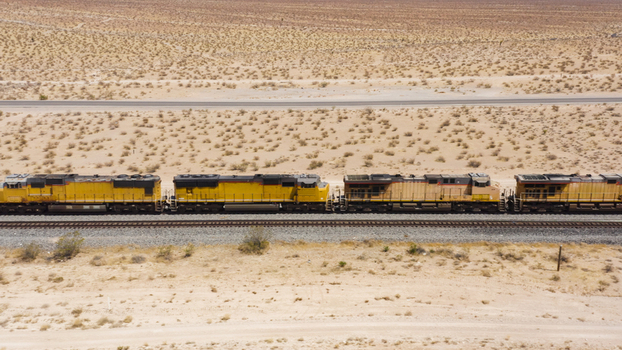 Aerial view of a yellow freight train traveling through the vast arid desert landscape in the United States.