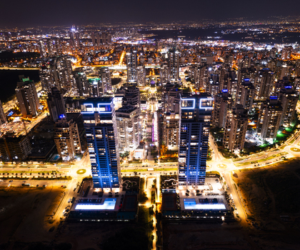 Aerial view of the illuminated skyline of Netanya at night featuring modern high rise towers glowing windows urban street lights and swimming pools Netanya Center District Israel. Aerial view of the illuminated skyline of Netanya at night featuring modern high rise towers glowing windows urban street lights and swimming pools Netanya Center District Israel.