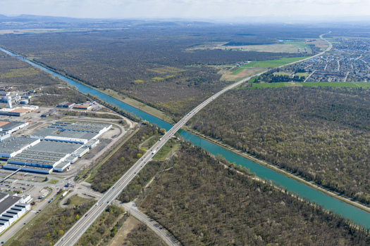 Aerial view of the shimmering canal dissecting the landscape contrasting with the dense forest and industrial buildings Sausheim Grand Est France.
