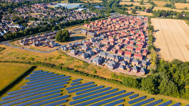 Aerial view of a modern residential housing development next to a large solar farm with rows of panels in the foreground and green fields in Dorset England United Kingdom. Aerial view of a modern residential housing development next to a large solar farm with rows of panels in the foreground and green fields in Dorset England United Kingdom.