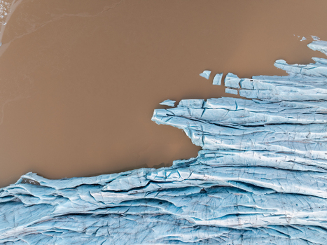 Aerial view of Svinafellsjokull glacier tongue with deep blue crevasses meeting the murky glacial meltwater lake in Sveitarfelagid Hornafjordur Iceland. Aerial view of Svinafellsjokull glacier tongue with deep blue crevasses meeting the murky glacial meltwater lake in Sveitarfelagid Hornafjordur Iceland.