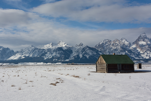 View of the historic Moulton Barn in Jackson Hole set against the snow capped Teton mountain range under a cloudy sky in Teton County Wyoming United States.