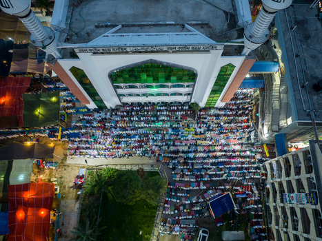 Aerial view of rows of people praying beneath the grand mosque with its white minarets reaching towards the sky Charmonai Barisal Division Bangladesh. Aerial view of rows of people praying beneath the grand mosque with its white minarets reaching towards the sky Charmonai Barisal Division Bangladesh.