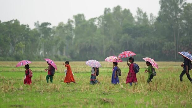 View of children with umbrellas walking through fields Bangladesh.