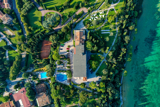 Aerial view of Villa Cortine Palace Hotel featuring lush gardens swimming pools and a tennis court on the shores of Lake Garda in Sirmione Lombardia Italy. Aerial view of Villa Cortine Palace Hotel featuring lush gardens swimming pools and a tennis court on the shores of Lake Garda in Sirmione Lombardia Italy.