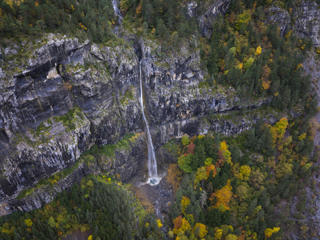 Aerial view of the Pyrenees waterfall cascading down rocky cliffs surrounded by vibrant autumn forests in Spain. Aerial view of the Pyrenees waterfall cascading down rocky cliffs surrounded by vibrant autumn forests in Spain.