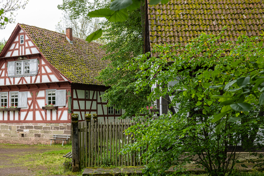 View of the historic half timbered buildings at Hennebergisches Museum Kloster Vessra with mossy tiled roofs and lush green trees in Kloster Vessra Thuringen Germany.