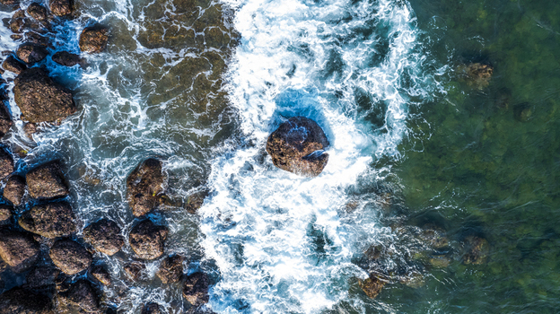 Aerial view of ocean waves crashing against dark rocks along the coastline in Bajawa Nusa Tenggara Timur Indonesia. Aerial view of ocean waves crashing against dark rocks along the coastline in Bajawa Nusa Tenggara Timur Indonesia.