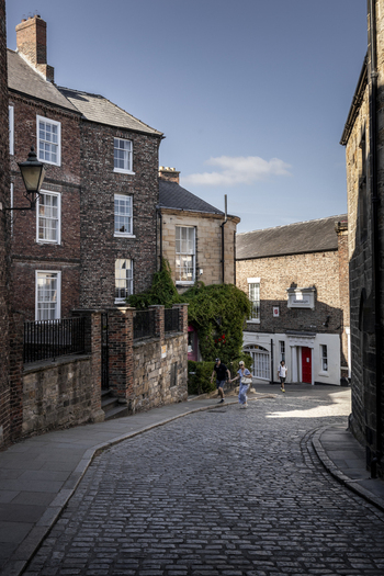 Durham England United Kingdom 13 July 2026 View of a historic cobblestone street in Durham with traditional brick buildings climbing ivy and people walking under a clear sky. Durham England United Kingdom 13 July 2026 View of a historic cobblestone street in Durham with traditional brick buildings climbing ivy and people walking under a clear sky.