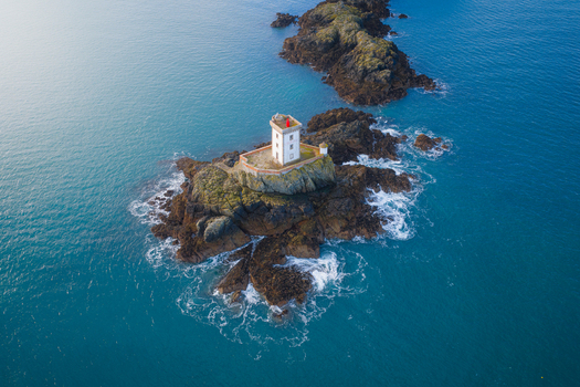 Aerial view of Phare de l Ost Pic lighthouse standing on a rocky islet surrounded by turquoise sea water and dark reef formations Plouezec France. Aerial view of Phare de l Ost Pic lighthouse standing on a rocky islet surrounded by turquoise sea water and dark reef formations Plouezec France.