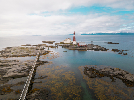 Aerial view of Tranoy Lighthouse situated on a rocky island with a long footbridge surrounded by the calm sea and distant mountains in Tranoy Nordland Norway. Aerial view of Tranoy Lighthouse situated on a rocky island with a long footbridge surrounded by the calm sea and distant mountains in Tranoy Nordland Norway.