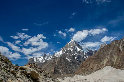 View of Trango Towers rising above a rocky mountain landscape under a bright blue sky with scattered clouds in Pakistan. View of Trango Towers rising above a rocky mountain landscape under a bright blue sky with scattered clouds in Pakistan.