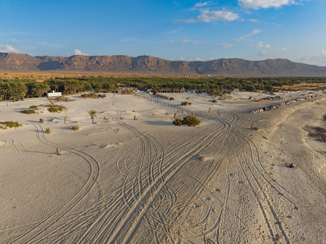 Aerial view of the textured sands stretch towards a verdant oasis framed by rugged mountains under a serene sky Kadrihnitin Socotra Yemen. Aerial view of the textured sands stretch towards a verdant oasis framed by rugged mountains under a serene sky Kadrihnitin Socotra Yemen.