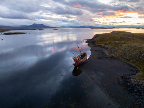 Aerial view of a shipwreck resting on a dark shore with still waters reflecting the colorful sunset sky and distant mountains Snæfellsnes Eyja og Miklaholtshreppur Iceland. Aerial view of a shipwreck resting on a dark shore with still waters reflecting the colorful sunset sky and distant mountains Snæfellsnes Eyja og Miklaholtshreppur Iceland.