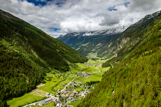 Aerial view of the village of Prutz nestled in a lush green valley surrounded by steep pine covered mountains and snow capped peaks under a cloudy sky in Prutz Tyrol Austria. Aerial view of the village of Prutz nestled in a lush green valley surrounded by steep pine covered mountains and snow capped peaks under a cloudy sky in Prutz Tyrol Austria.