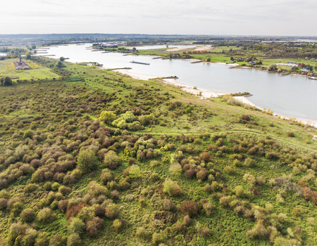 Aerial view of the Millingerwaard nature reserve featuring lush greenery autumn foliage and the winding Waal river with a cargo barge in Kekerdom Gelderland Netherlands.
