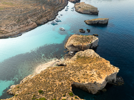 Aerial view of turquoise waters meet rugged cliffs and boats dot the horizon in the serene Blue Lagoon Comino Malta. Aerial view of turquoise waters meet rugged cliffs and boats dot the horizon in the serene Blue Lagoon Comino Malta.