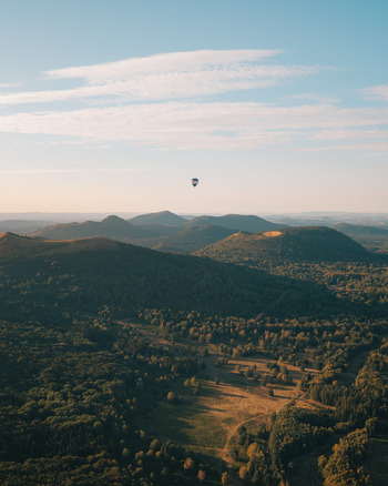 Aerial view of a hot air balloon floating above the volcanic landscape of Puy de Dome during golden hour in Orcines Auvergne Rhone Alpes France.