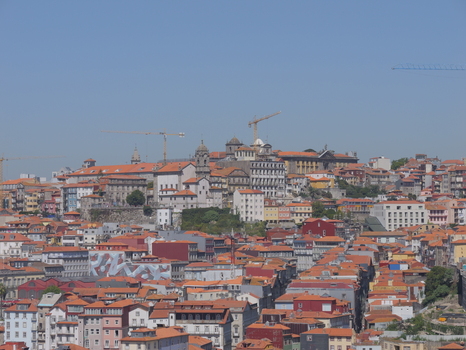 View of the historic cityscape of Porto with its iconic orange tiled rooftops traditional architecture and construction cranes under a clear blue sky in Porto Porto District Portugal. View of the historic cityscape of Porto with its iconic orange tiled rooftops traditional architecture and construction cranes under a clear blue sky in Porto Porto District Portugal.