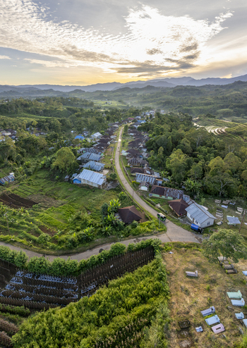 Aerial view of Bangka Kenda village nestled among lush green hills terraced fields and tropical vegetation under a soft sunset sky in Wae Rii East Nusa Tenggara Indonesia.