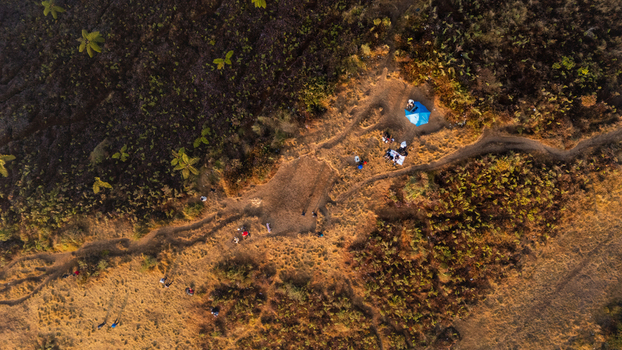 Aerial view of the Sunrise Camp Gunung Prau area with a blue tent and hikers on a mountain trail surrounded by dry grassy terrain in Kecamatan Kejajar Jawa Tengah Indonesia.