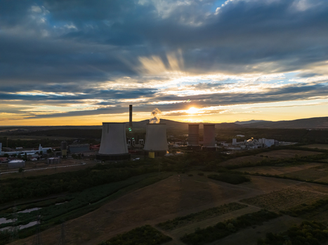Aerial view of the Matra power plant with cooling towers and a chimney releasing steam at sunset amid farmland and the Matra hills near Visonta Hungary.