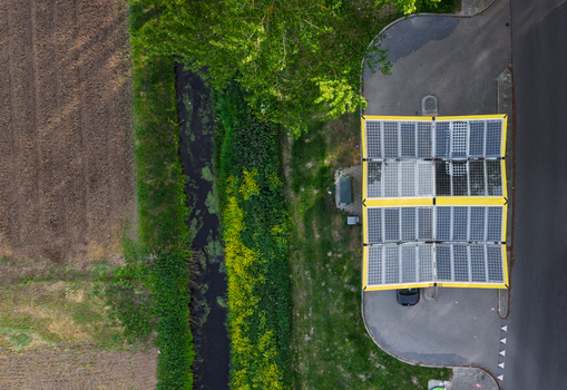 Aerial view of the Fastned Charging Station with its distinctive yellow solar panel roof located next to a narrow canal and green fields Vierpolders Zuid Holland Netherlands. Aerial view of the Fastned Charging Station with its distinctive yellow solar panel roof located next to a narrow canal and green fields Vierpolders Zuid Holland Netherlands.