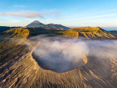 Aerial view of Mount Bromo sunrise featuring the volcanic crater rim with rising steam and golden light illuminating the rugged landscape in Tosari East Java Indonesia.