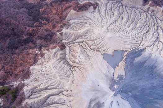 Aerial view of the Vulcanii Noroiosi Paclele Mari mud volcanoes with intricate grey clay patterns eroded channels and surrounding autumn vegetation in Paclele Buzau County Romania.