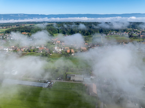 Aerial view of the village partially covered by morning mist with green fields and distant mountains in Grossaffoltern Canton of Bern Switzerland. Aerial view of the village partially covered by morning mist with green fields and distant mountains in Grossaffoltern Canton of Bern Switzerland.