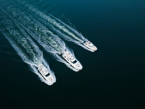 Aerial view of three white yachts cruising in parallel across deep blue water with prominent white wakes in Panaji Goa India.