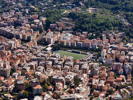 Aerial view of the urban landscape featuring dense residential buildings a green sports field and lush hillsides under bright daylight Rapallo Liguria Italy. Aerial view of the urban landscape featuring dense residential buildings a green sports field and lush hillsides under bright daylight Rapallo Liguria Italy.