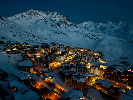 Aerial view of a radiant village nestled amongst the snow clad mountains where golden lights dance against the cold twilight Val Thorens Auvergne Rh&ocirc;ne Alpes France.
