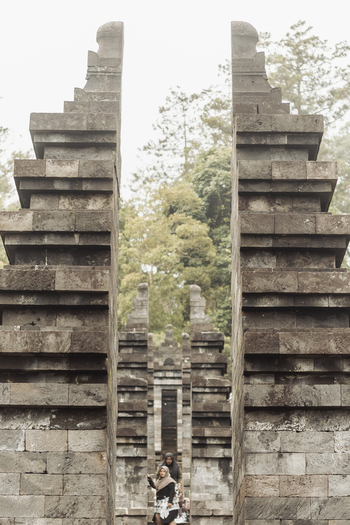 View of Cetho Temple with its iconic split stone gateway and people walking through the ancient complex surrounded by misty forest Kecamatan Jenawi Jawa Tengah Indonesia. View of Cetho Temple with its iconic split stone gateway and people walking through the ancient complex surrounded by misty forest Kecamatan Jenawi Jawa Tengah Indonesia.