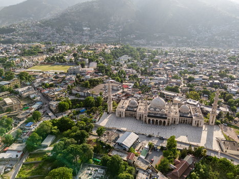 Aerial view of the Central Mosque with its domes and minarets surrounded by dense urban buildings lush trees and mountainous terrain in Muzaffarabad Azad Kashmir Pakistan. Aerial view of the Central Mosque with its domes and minarets surrounded by dense urban buildings lush trees and mountainous terrain in Muzaffarabad Azad Kashmir Pakistan.