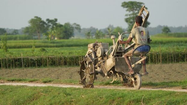 View of a farmer driving a power tiller through rural fields Bangladesh. View of a farmer driving a power tiller through rural fields Bangladesh.