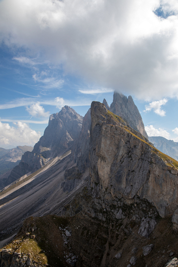 View of the jagged peaks of the Dolomites with steep rocky slopes and green ridges under a blue sky with white clouds Rocca Pietore Veneto Italy. View of the jagged peaks of the Dolomites with steep rocky slopes and green ridges under a blue sky with white clouds Rocca Pietore Veneto Italy.