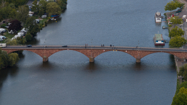 Aerial view of the Mainbrucke stone arch bridge spanning the Main river with cars and pedestrians crossing surrounded by trees and boats in Miltenberg Bayern Germany.