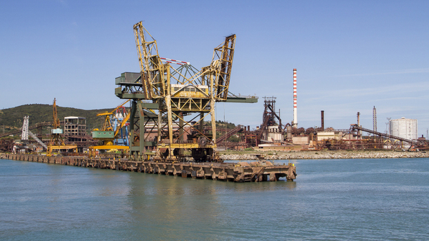 View of a colossal weathered crane looming over the tranquil cerulean waters juxtaposed against the industrial skyline Piombino Tuscany Italy. View of a colossal weathered crane looming over the tranquil cerulean waters juxtaposed against the industrial skyline Piombino Tuscany Italy.