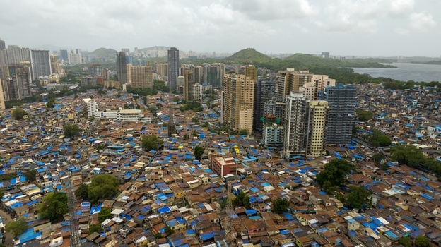 Aerial view of Dharavi Slums with dense low rise housing featuring blue tarpaulin roofs contrasted against modern high rise apartment buildings in Mumbai Maharashtra India. Aerial view of Dharavi Slums with dense low rise housing featuring blue tarpaulin roofs contrasted against modern high rise apartment buildings in Mumbai Maharashtra India.