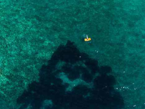 Aerial view of a person on a yellow inflatable mattress floating in the crystal clear turquoise waters of Aquarium Beach in Jala Vlore County Albania. Aerial view of a person on a yellow inflatable mattress floating in the crystal clear turquoise waters of Aquarium Beach in Jala Vlore County Albania.