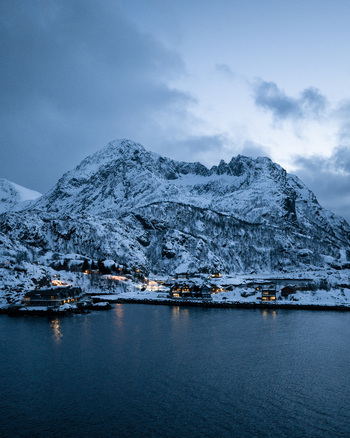 Aerial view of snow covered mountains and a village nestled along the tranquil waters lights twinkling against the fading light Hamn Troms Norway. Aerial view of snow covered mountains and a village nestled along the tranquil waters lights twinkling against the fading light Hamn Troms Norway.