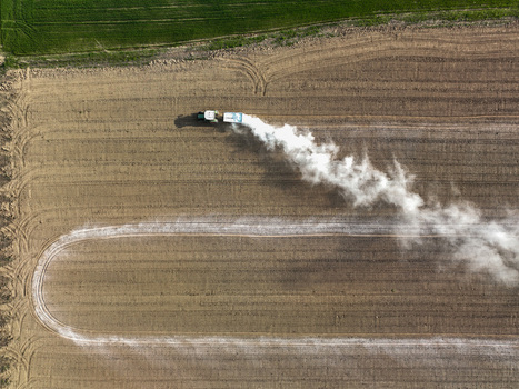 Aerial view of a tractor spreading white fertilizer across a tilled agricultural field with visible tire tracks Borgo d Ale Piedmont Italy.