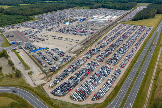 Aerial view of a large car logistics and storage facility with thousands of new vehicles parked in organized rows located near a highway in Mszczonow Masovian Voivodeship Poland.