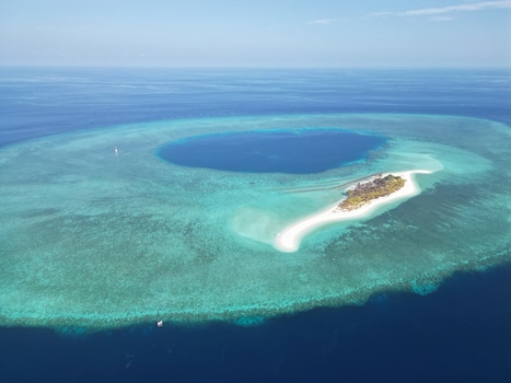 Aerial view of Pulau Ndaa surrounded by vibrant turquoise coral reefs and deep blue ocean waters Tomia South East Sulawesi Indonesia.