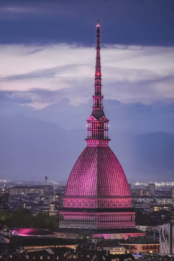 Aerial view of the Mole Antonelliana illuminated in pink light at dusk with the city skyline and Alps in the background Turin Piedmont Italy. Aerial view of the Mole Antonelliana illuminated in pink light at dusk with the city skyline and Alps in the background Turin Piedmont Italy.