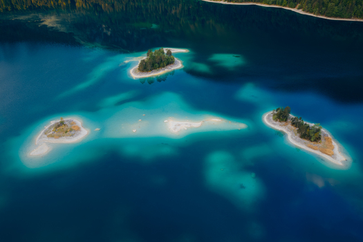 Aerial view of Eibsee lake featuring small islands and vibrant turquoise water surrounded by dense forest in Grainau Bavaria Germany. Aerial view of Eibsee lake featuring small islands and vibrant turquoise water surrounded by dense forest in Grainau Bavaria Germany.